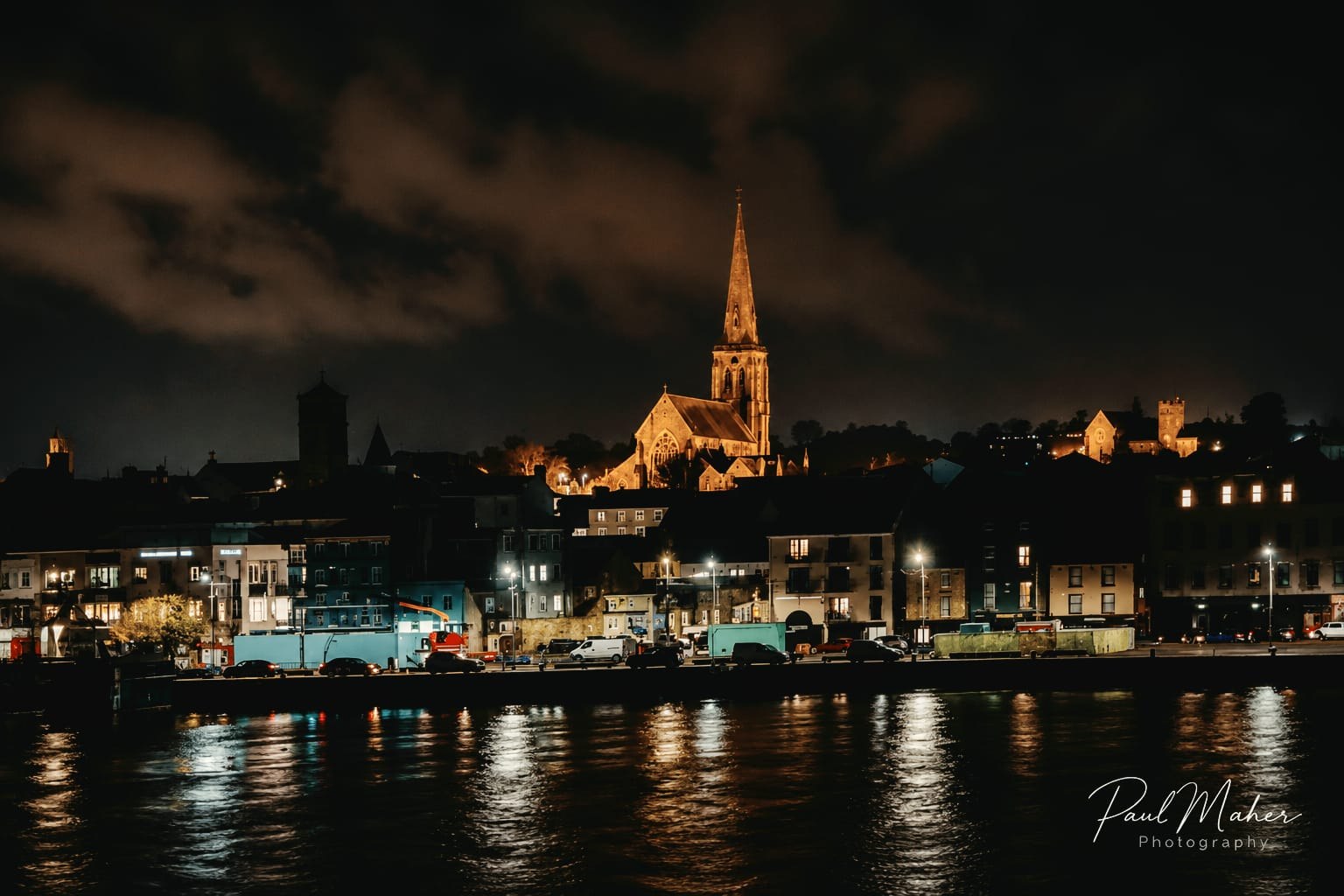 Town lights and a church spire reflected in the water at night