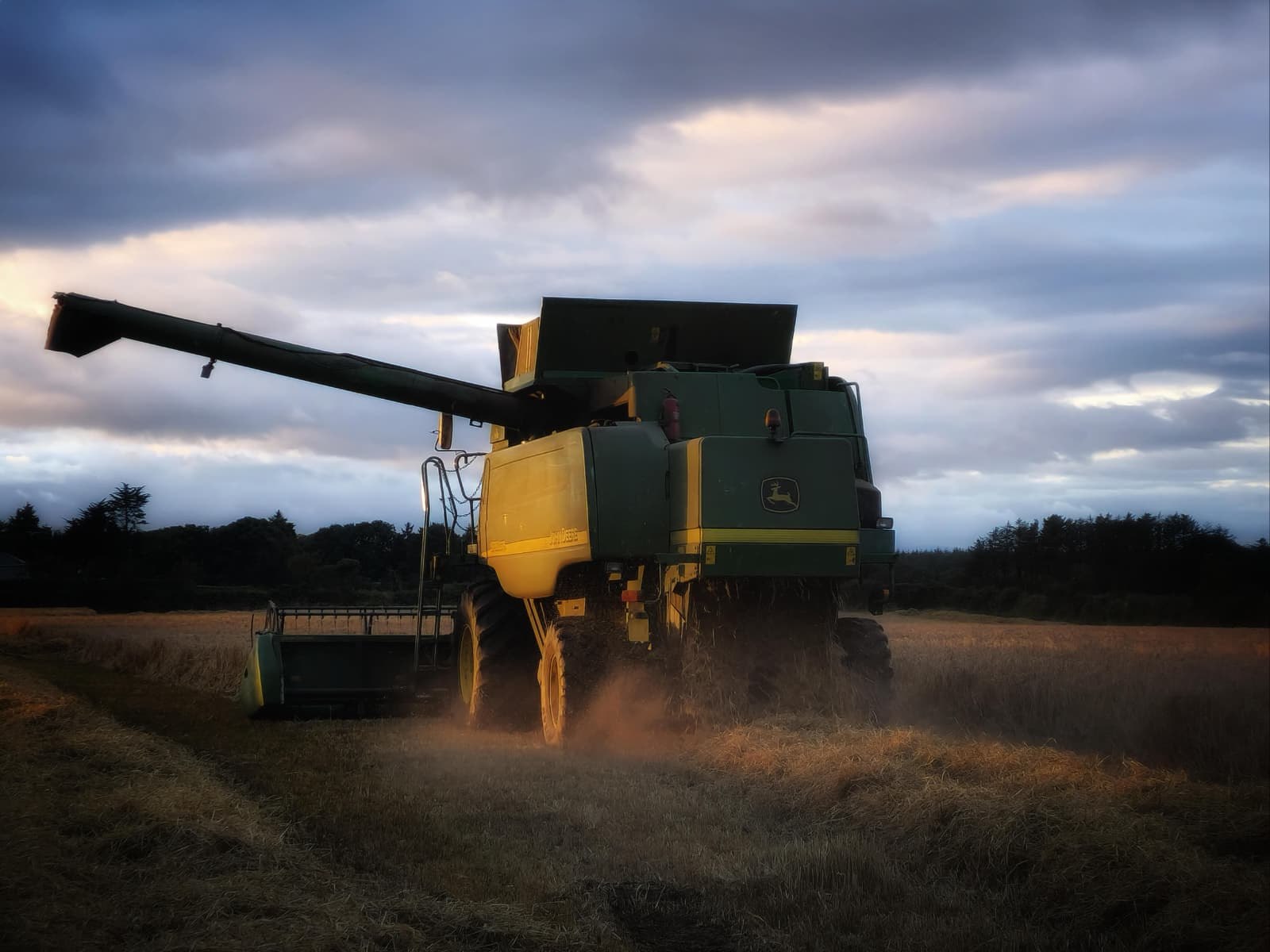 A combine harvester working a stubble field under a dusk sky