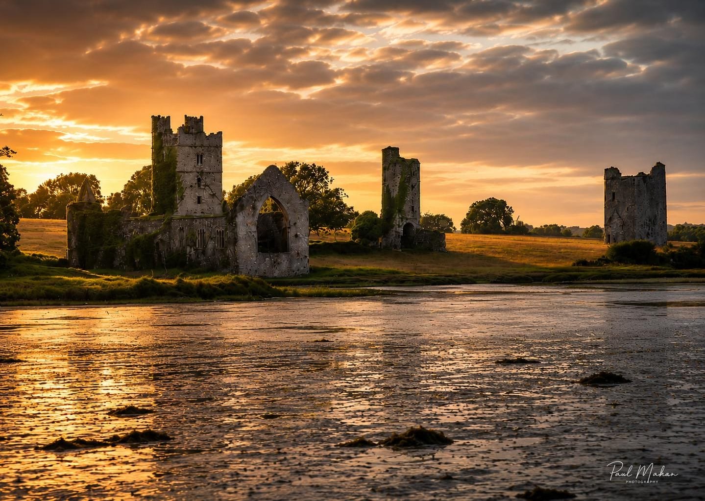 Ruined stone walls standing over still water at sunset