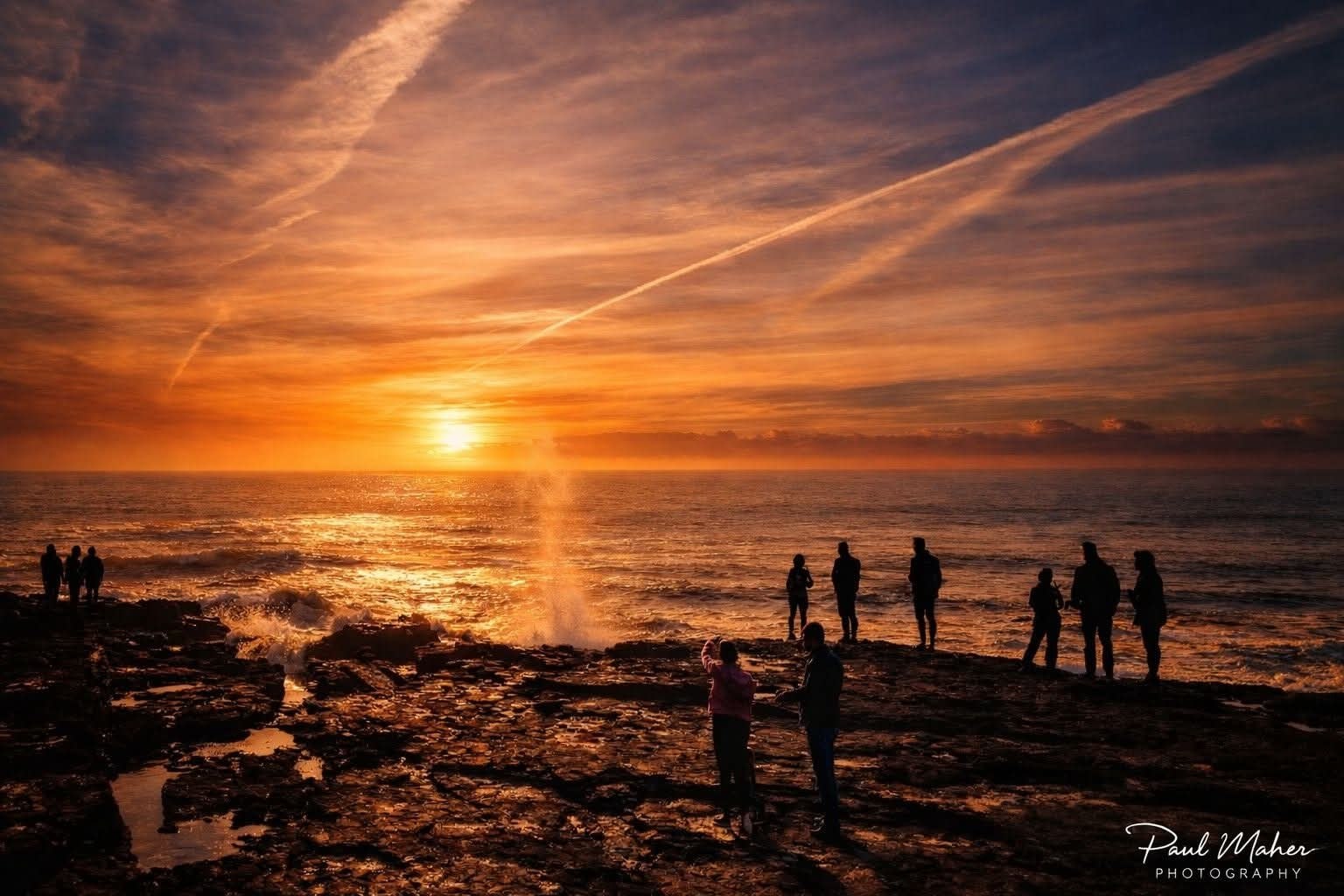 People silhouetted on a rocky shore as the sun sets over the sea